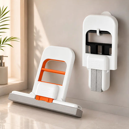 A wall-mounted white and orange squeezable mini mops are shown in a clean indoor room setting with sunlight, a plant, and a tiled floor.